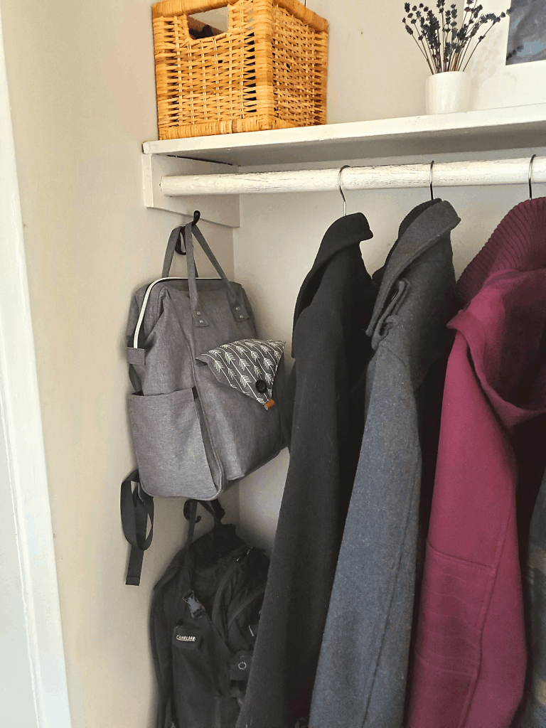 entryway closet with bags on hooks and coats on hangers