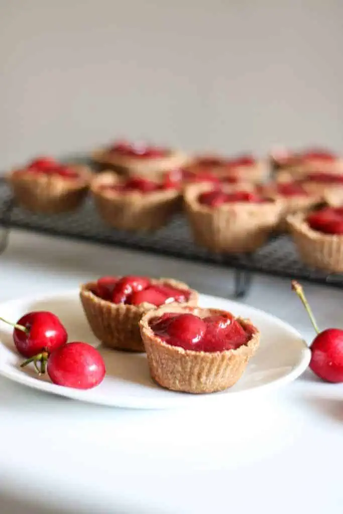 2 cherry tarts on a plate with more in the background on cooling rack