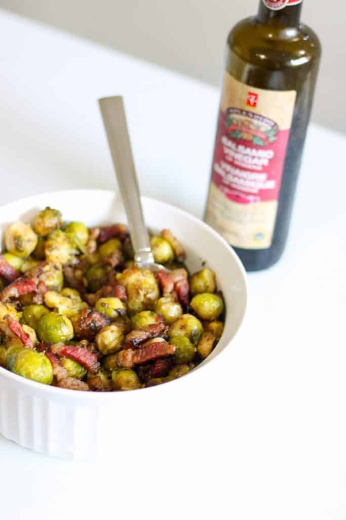 roasted brussels sprouts in serving dish with balsamic vinegar behind it