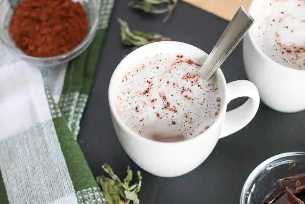 Cup of chocolate mint tea latte, with mint leaves scattered around and a bowl of cocoa powder