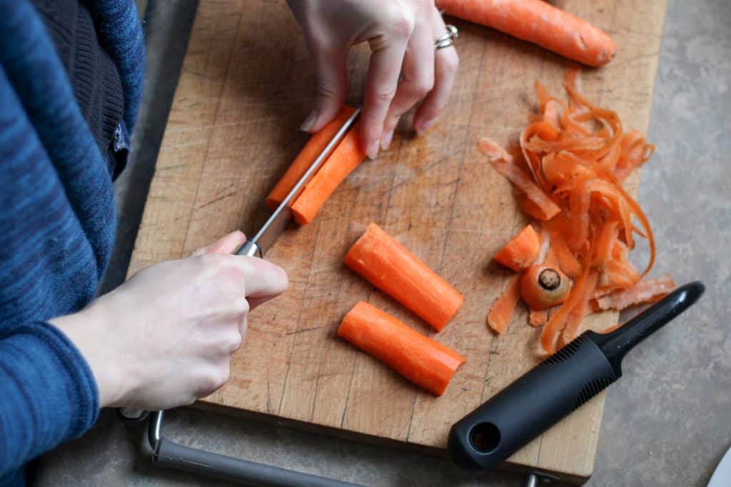 Woman cutting a carrot in half lengthwise in a cutting board