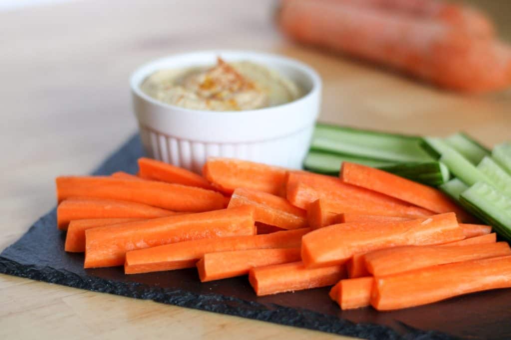 carrot sticks on a tray with cucumbers and a bowl of hummus