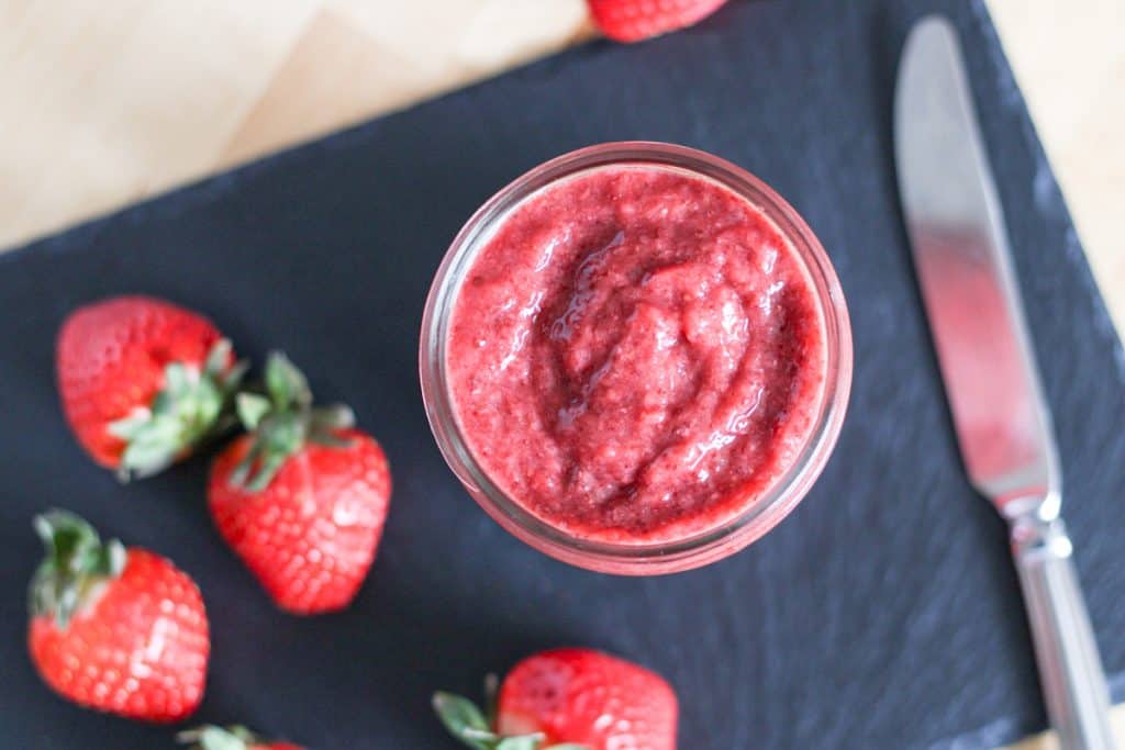 Strawberry jam in a jar, surrounded with fresh strawberries and a butter knife