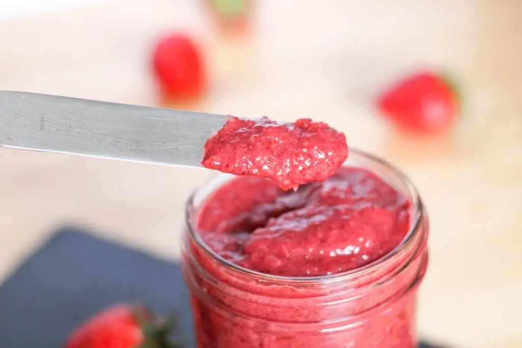 Scooping jam out of a jar with a butterknife