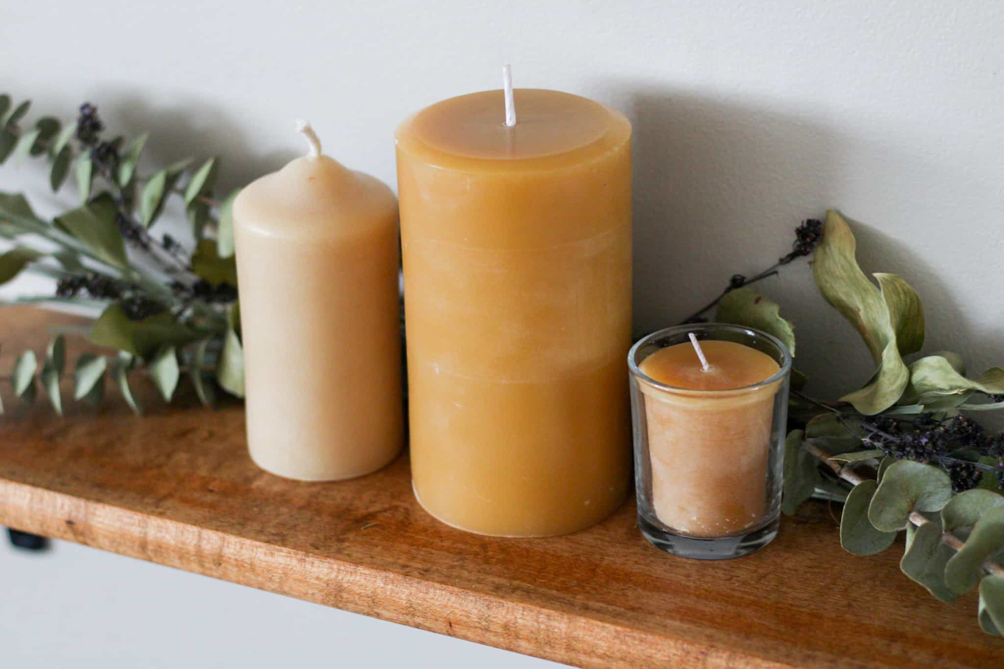 3 beeswax candles on shelf with greenery behind them