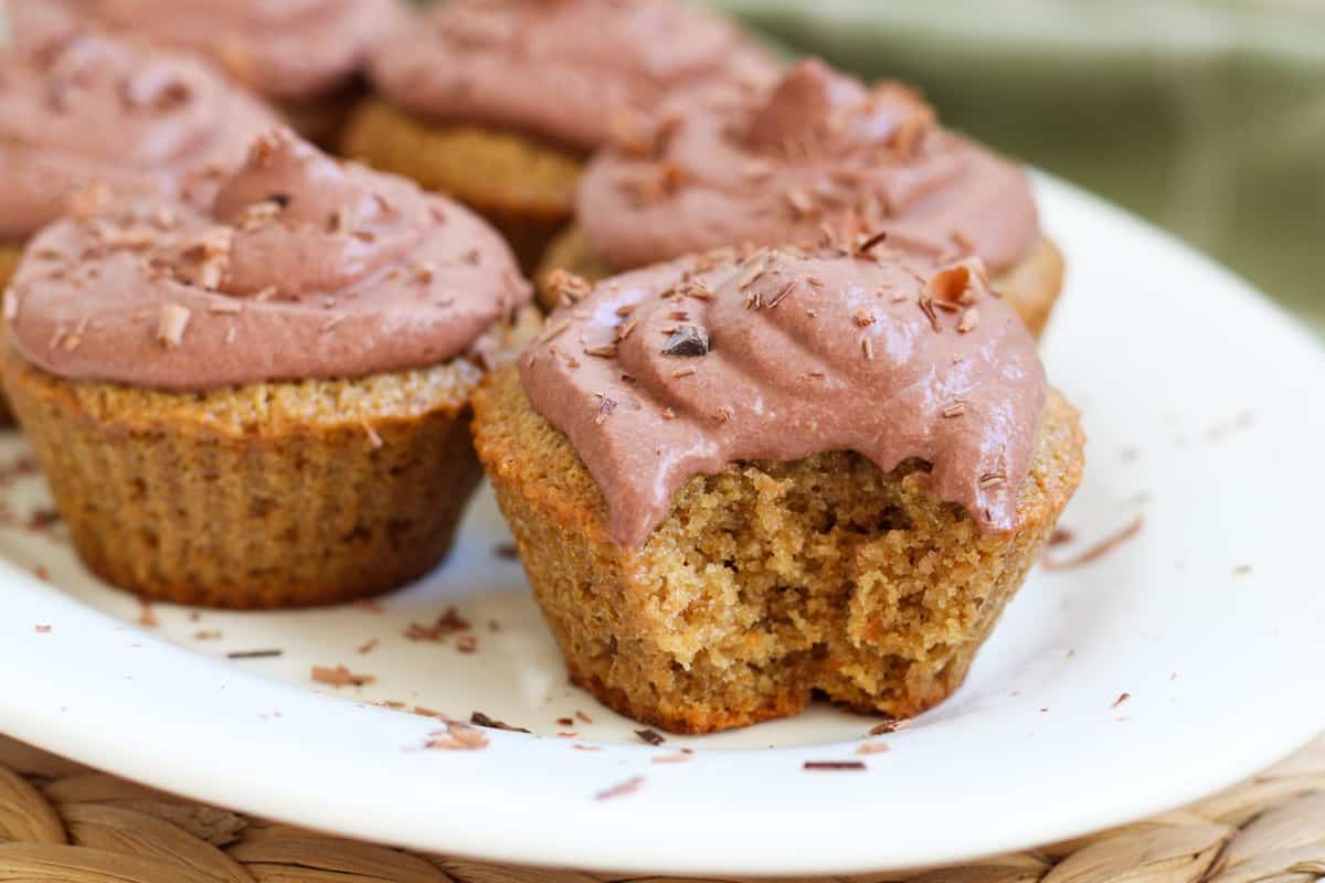 plate of vanilla cupcakes with chocolate frosting, one cupcake has a bite taken out