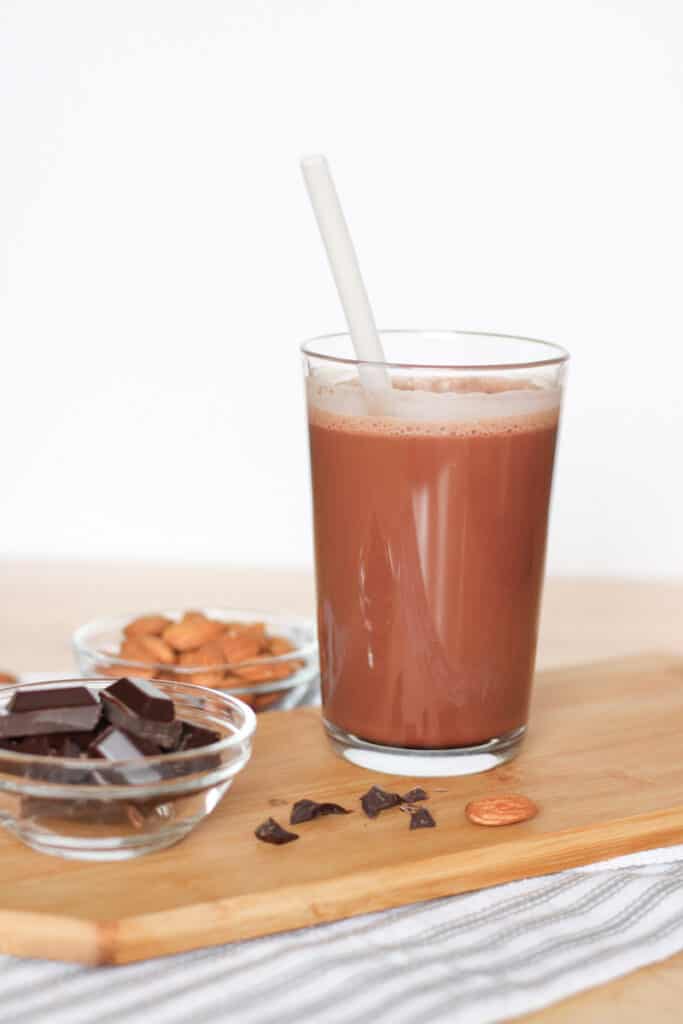 glass of chocolate milk on a board with chocolate chunks and almonds