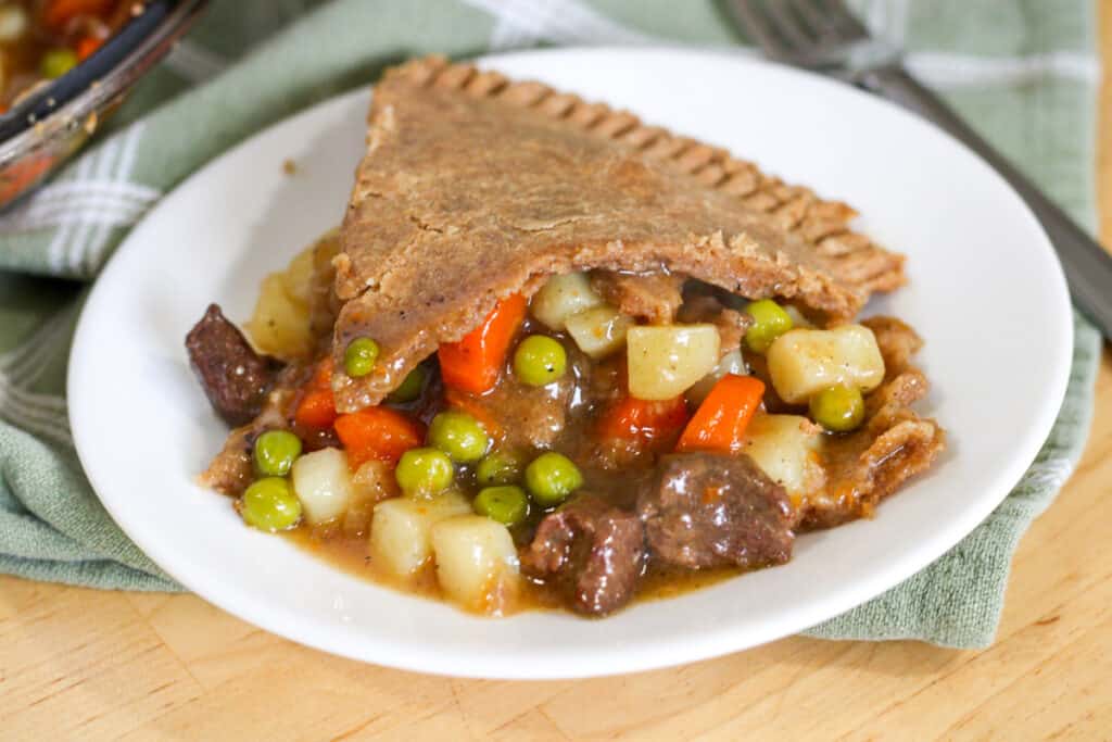 slice of beef pot pie on a plate with beef, potatoes, peas, carrots and crust