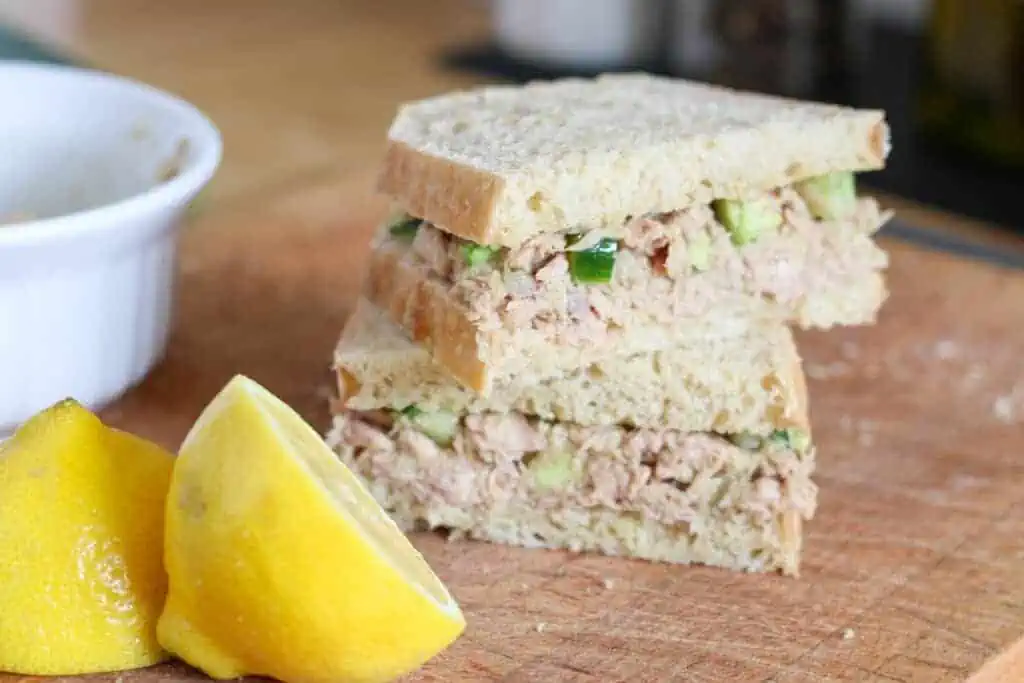 tuna salad sandwich cut in half, with lemons on the side
