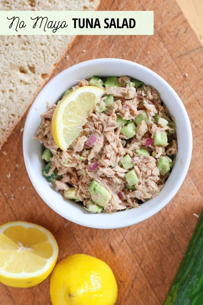 bowl of tuna salad with lemon slice, lemons, cucumber and bread