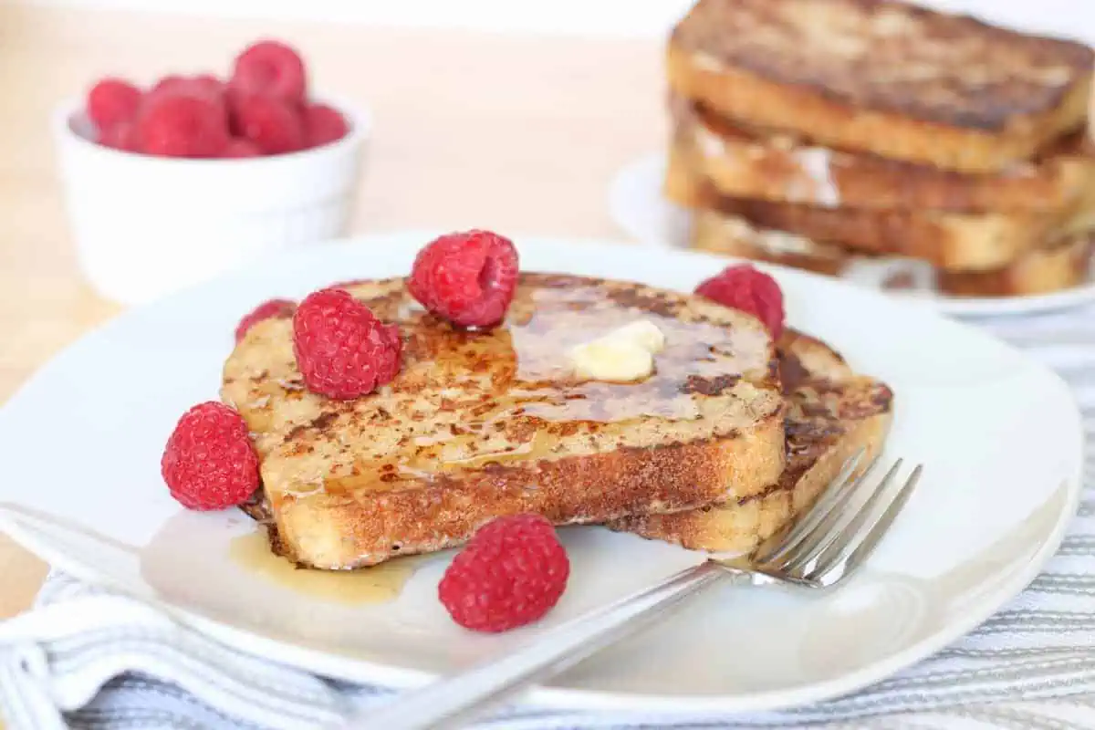 french toast on a plate with raspberries, syrup and butter