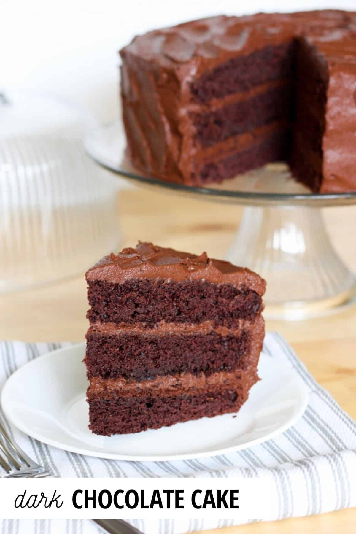 slice of dark chocolate cake on a plate with cake on cake stand in the background