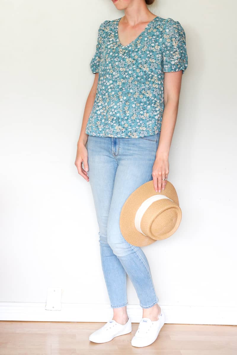 woman in floral shirt, light jeans and holding a hat