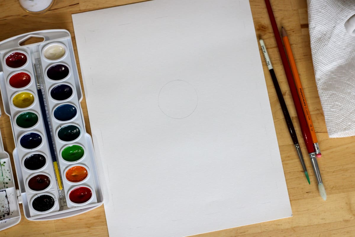 paper with a circle drawn in the middle with paints and brushes on the side