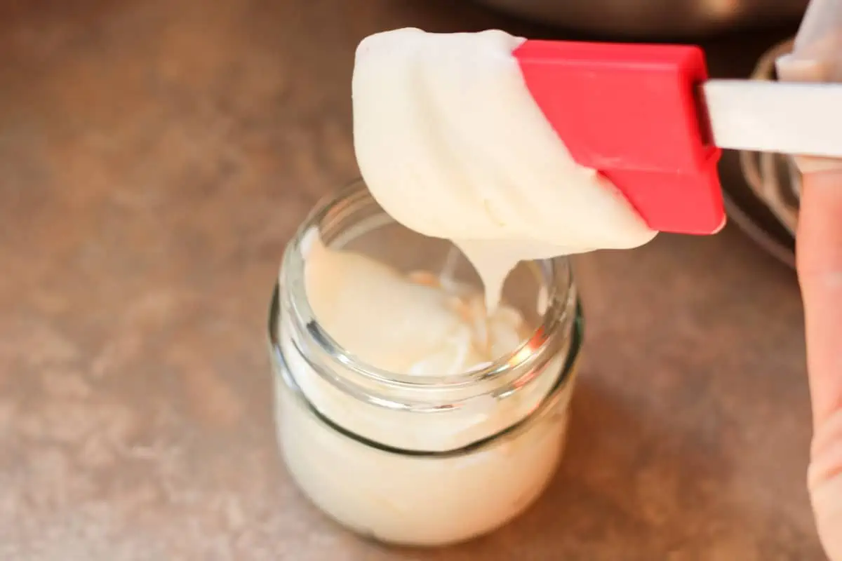putting tallow balm in a jar with a spatula