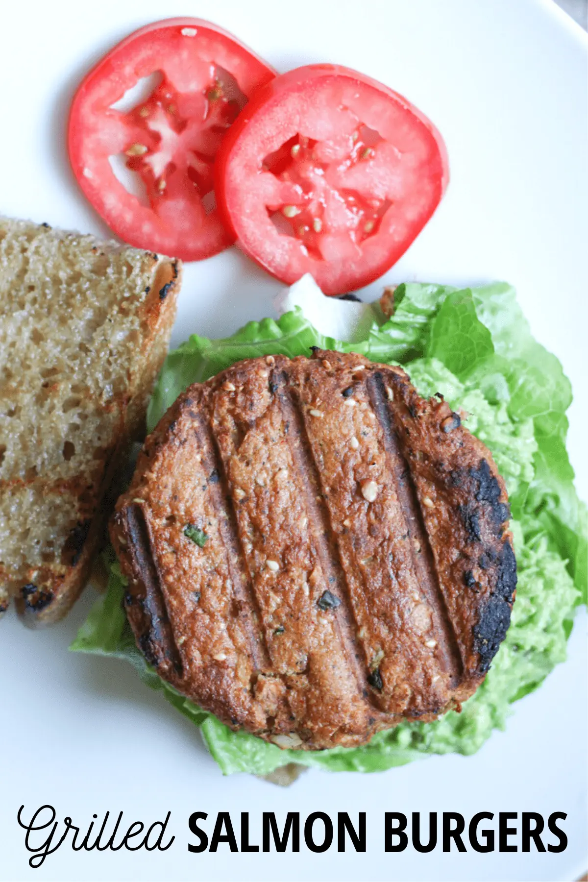 salmon burger on bread with lettuce and avocado, with tomatoes on the side