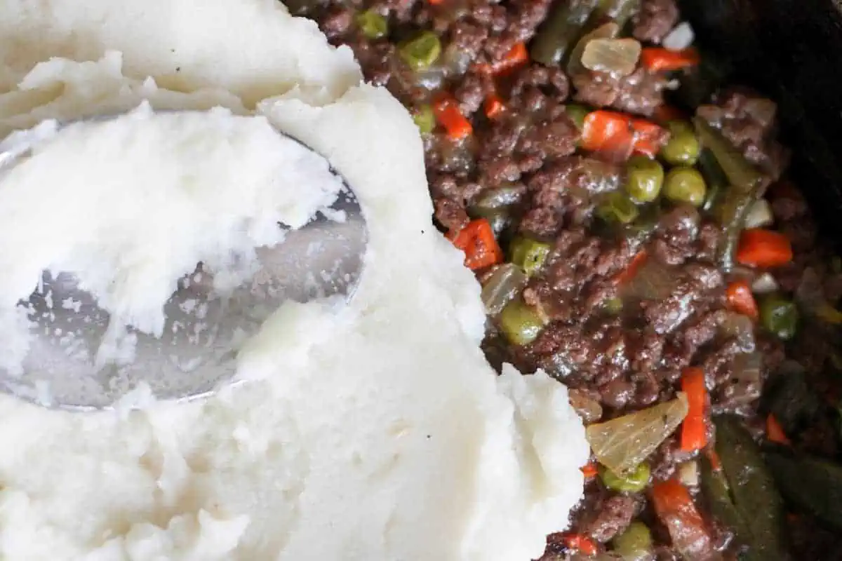 smoothing mashed potatoes on shepherd's pie meat mixture with a spoon