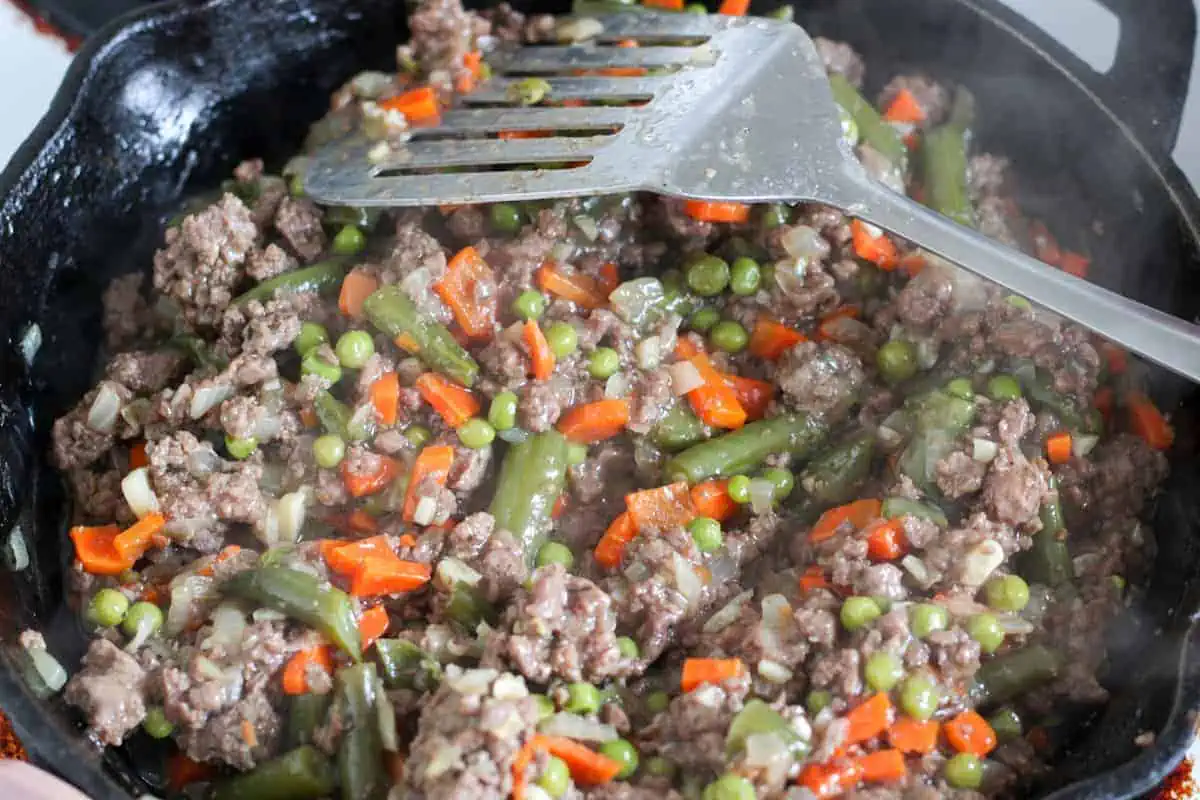 ground meat and veggie mixture in a pan with flipper