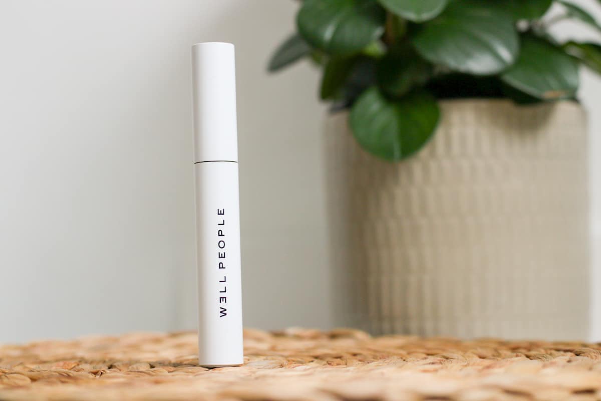 white mascara tube standing up in front of a plant