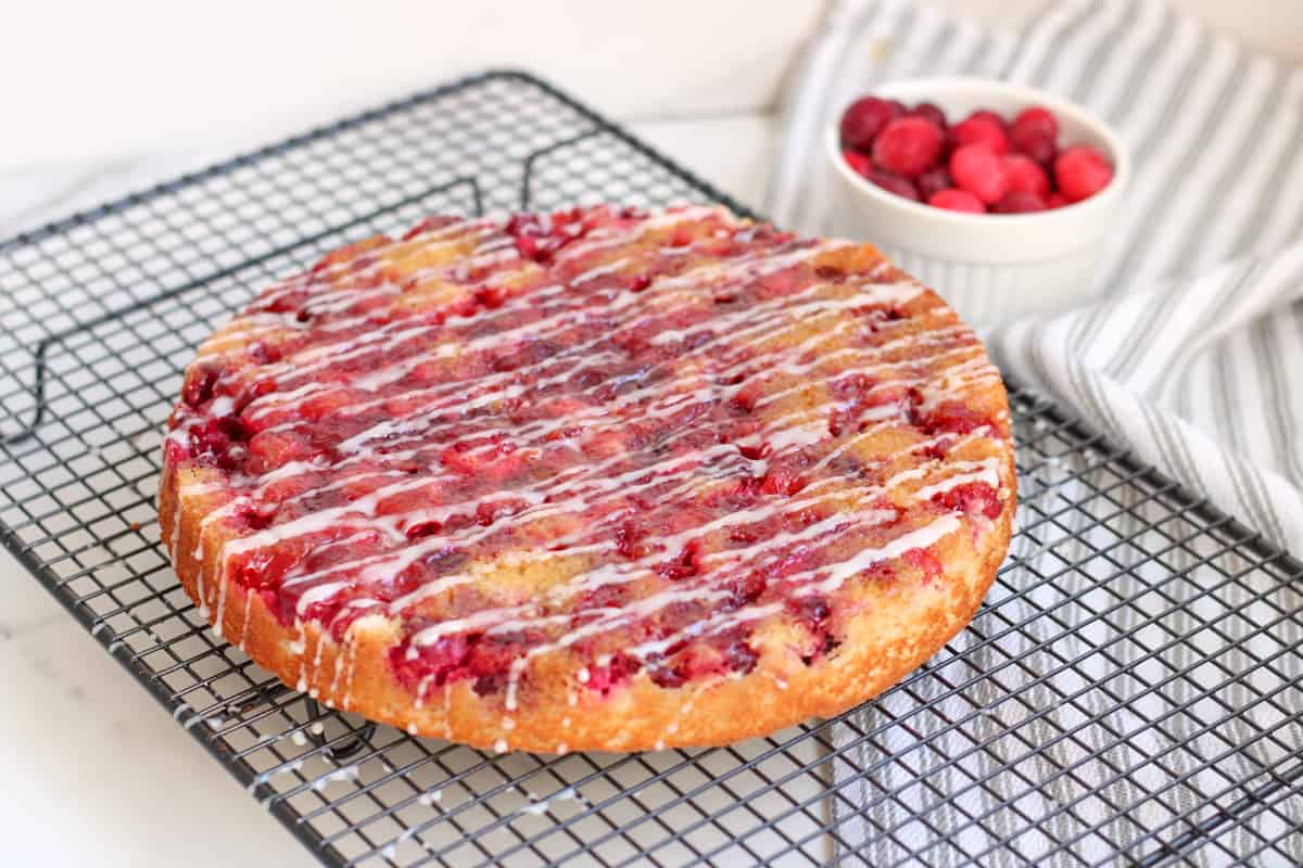 a cranberry cake with drizzle of icing on a cooling rack
