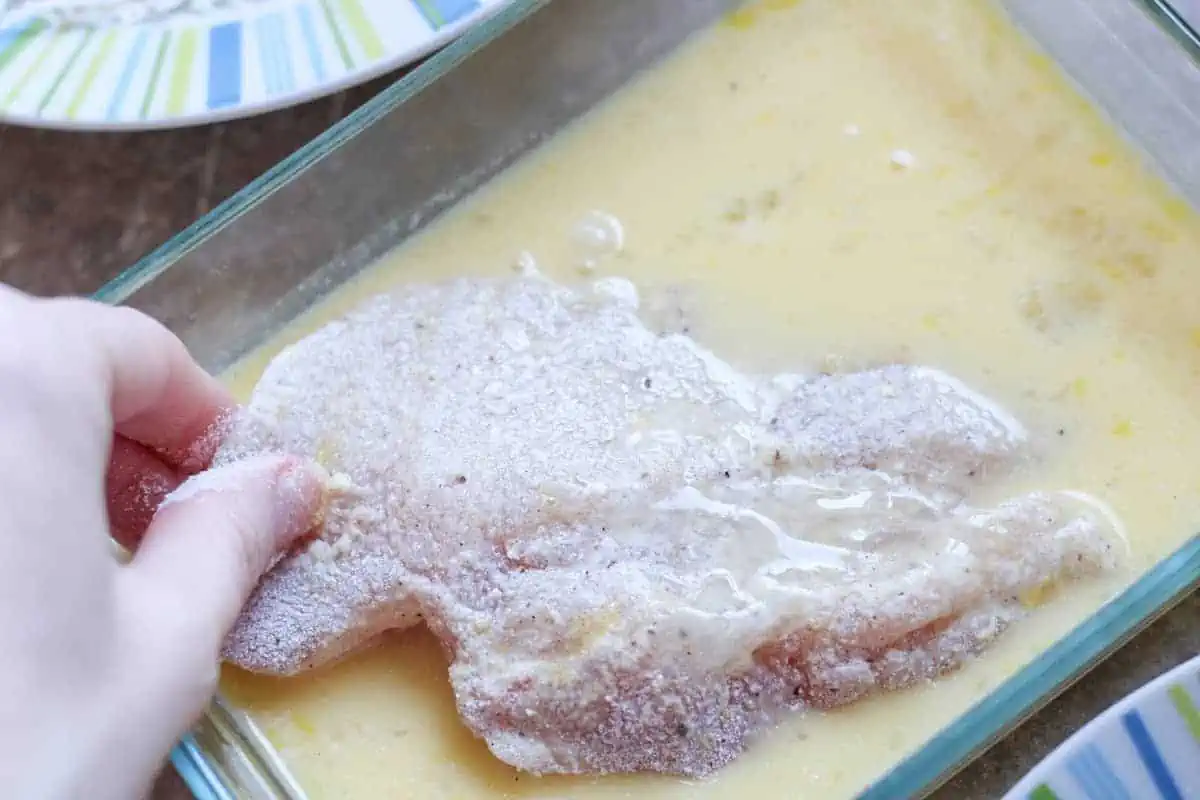 coating a breaded chicken breast with egg mixture