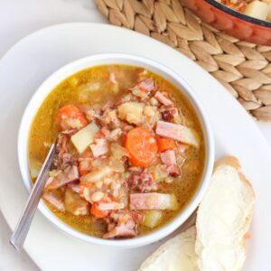 bowl of ham soup on a plate with bread slices