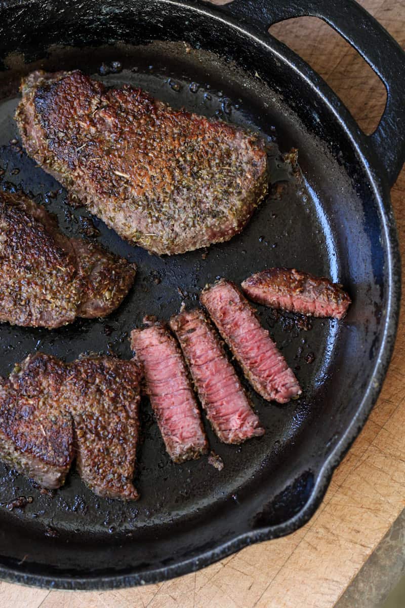 steaks in a cast iron pan on wood board
