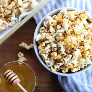 Bowl of golden honey popcorn beside small bowl of honey