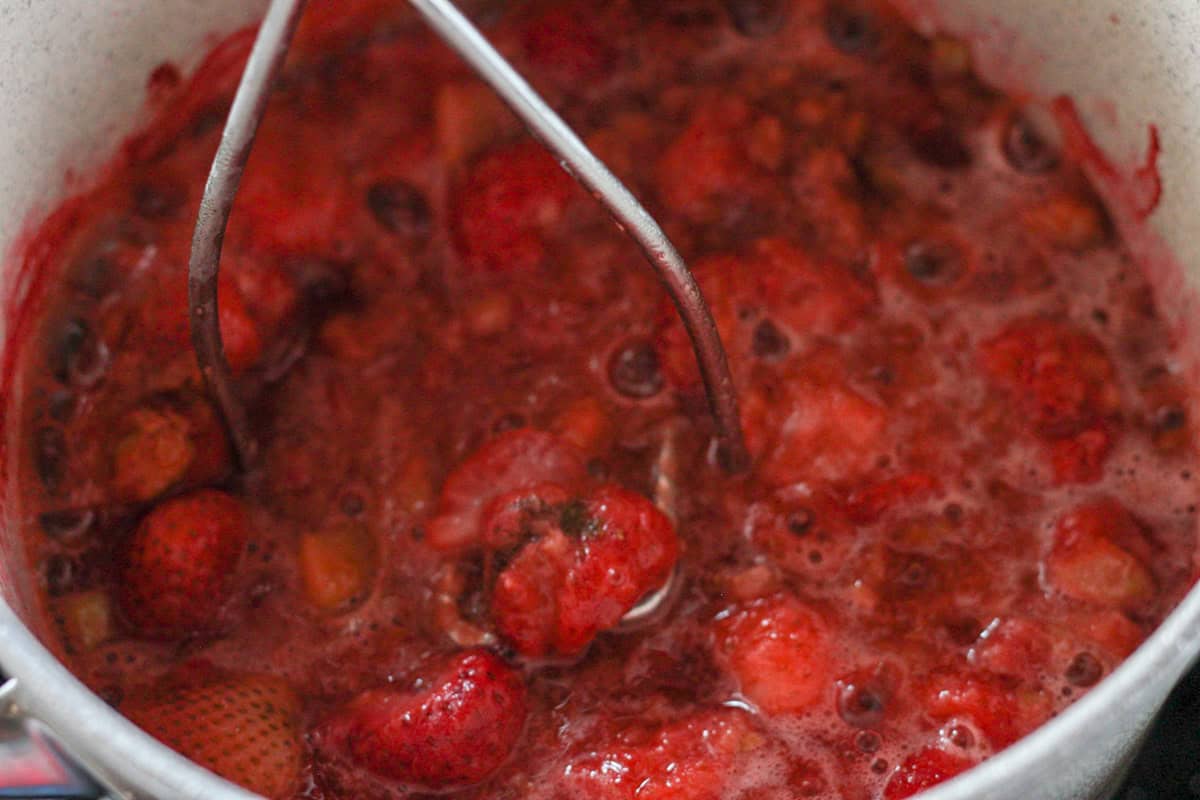 potato masher smashing strawberries and rhubarb in pot